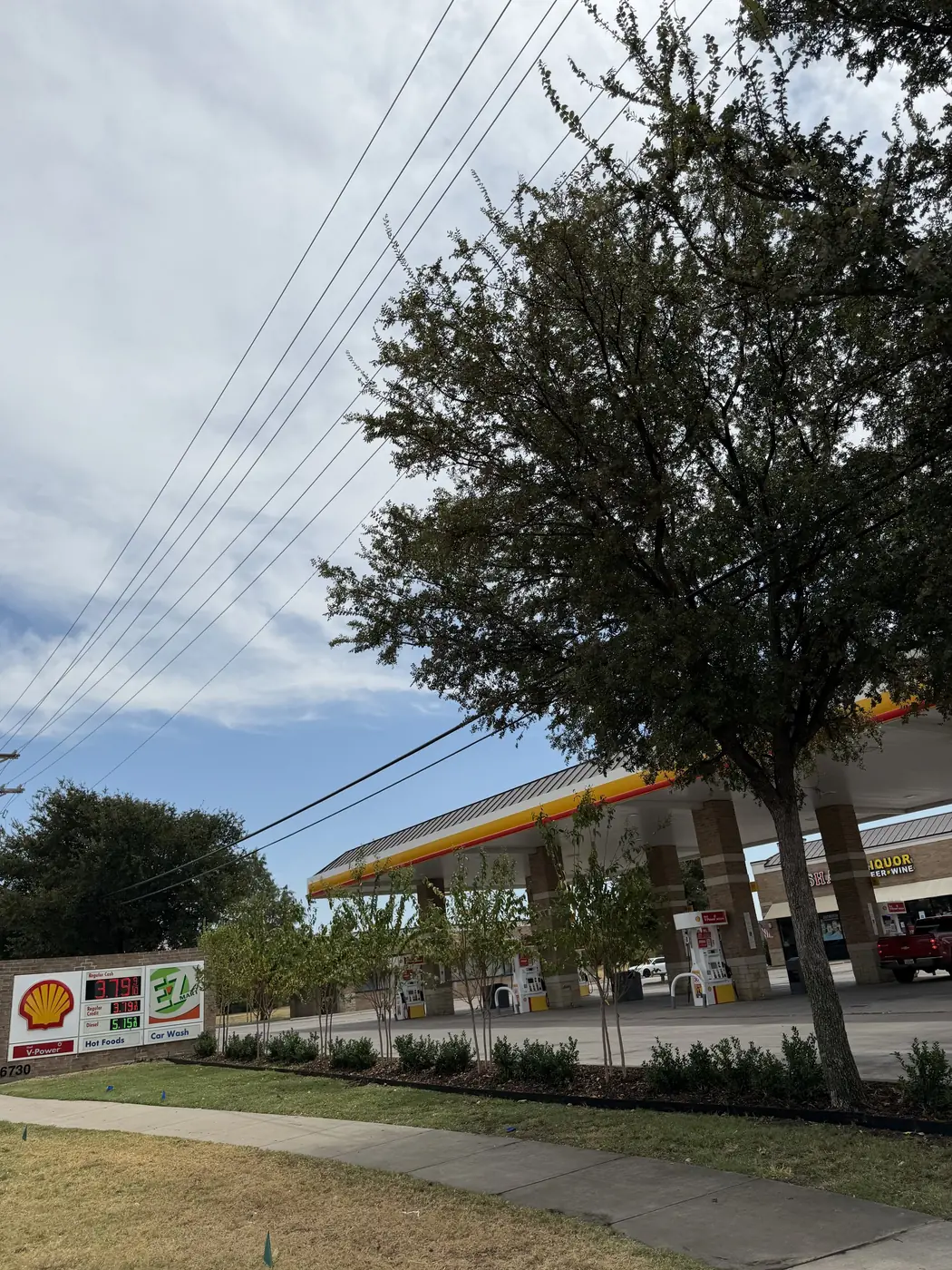 The finished frontage at a fuel station: newly planted crape myrtles and a clipped boxwood hedge in a mulched bed with steel edging, running the length of the sidewalk