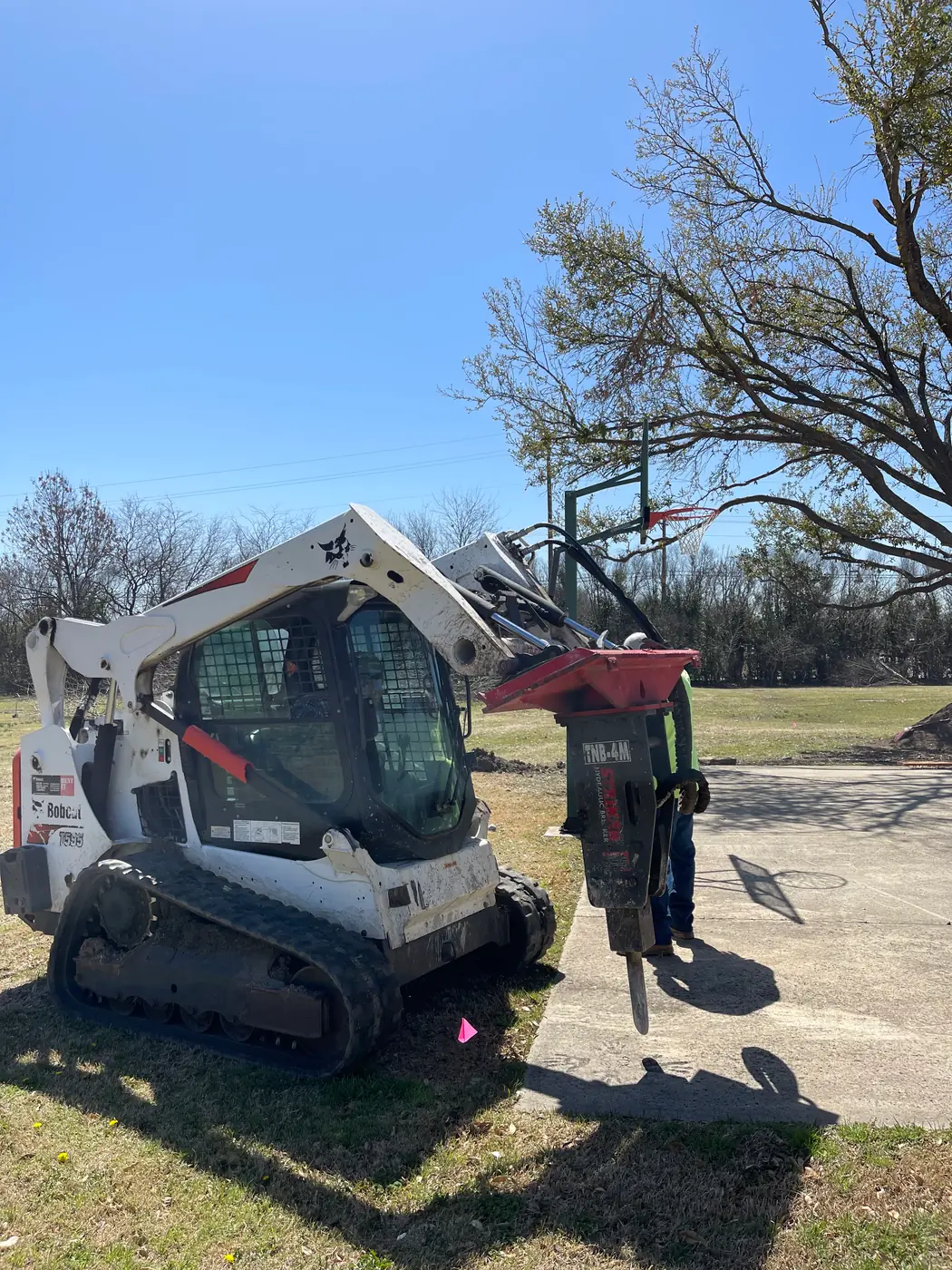 Bobcat T590 track loader with a TNB-4M hydraulic breaker positioned at the edge of a concrete slab, crew member alongside