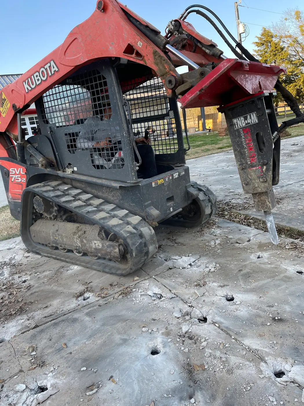 Kubota SVL75-2 track loader running a TNB-4M hydraulic breaker through a concrete slab, broken holes and rubble across the surface