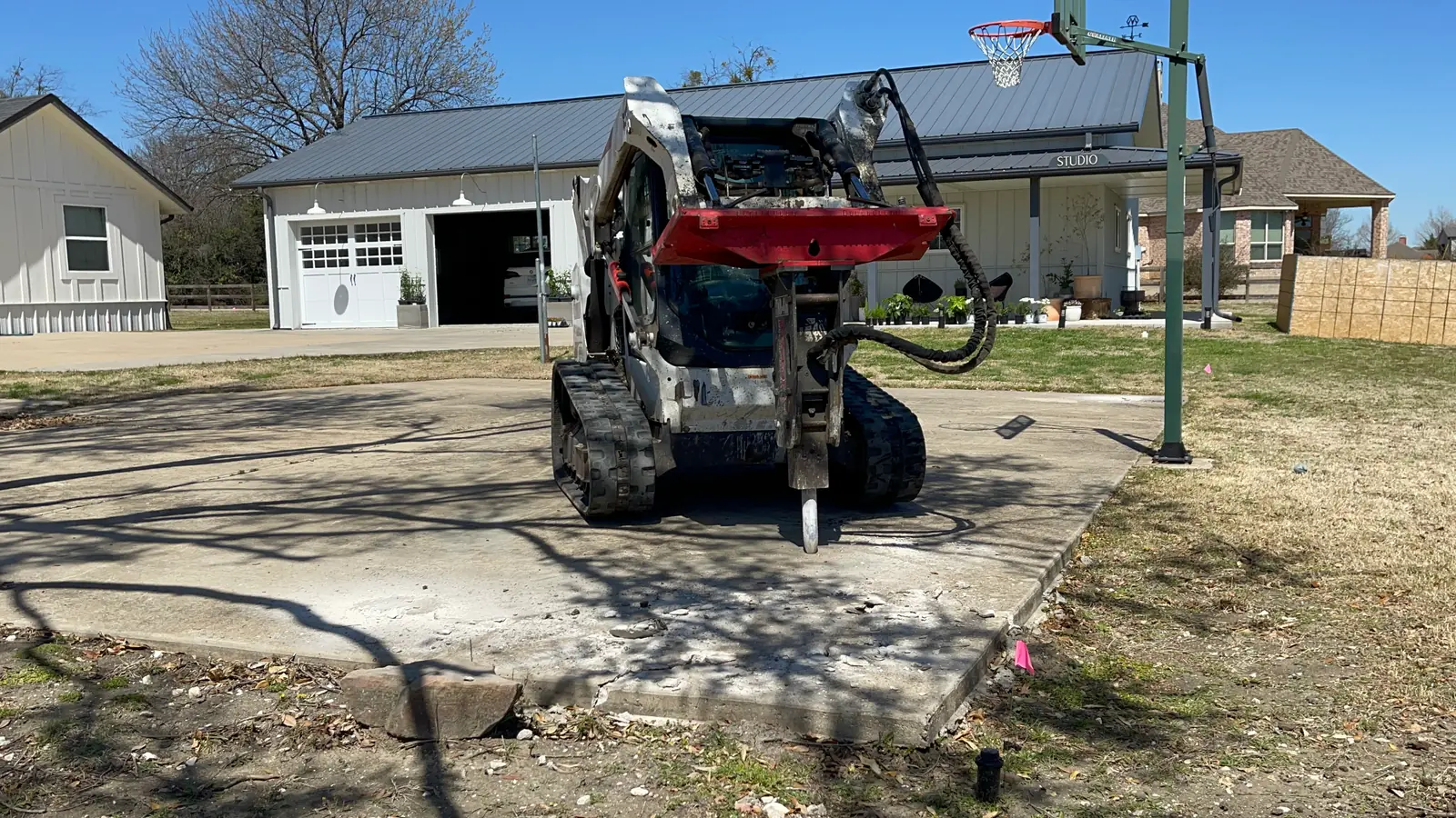 Track loader with a hydraulic breaker standing on an old residential concrete slab before demolition