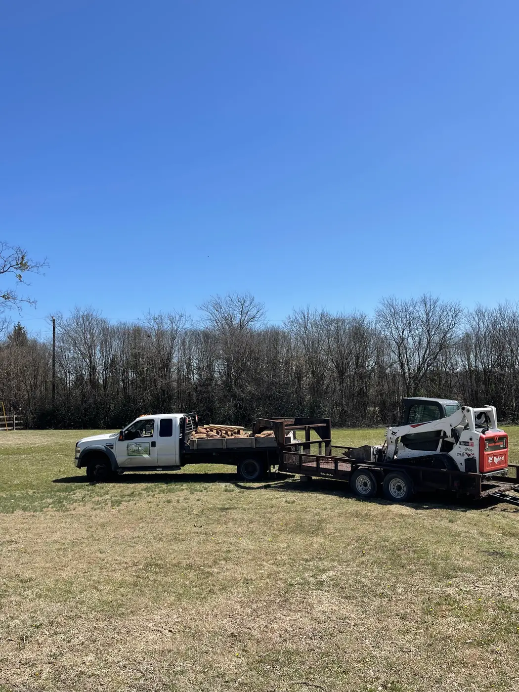 Flatbed truck loaded with broken concrete alongside a skid steer on a trailer at a North Texas property