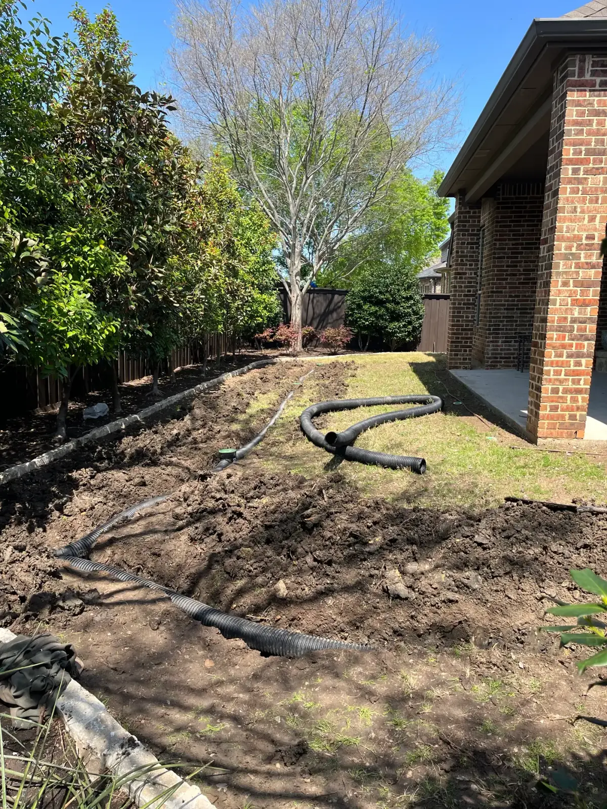 Open French drain trench with perforated pipe laid along the side of a North Texas brick home