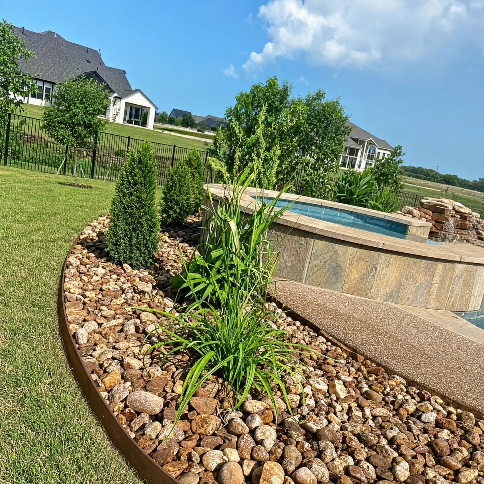 Curved river-rock bed with ornamental grasses beside a pool, Godoy's Wolves