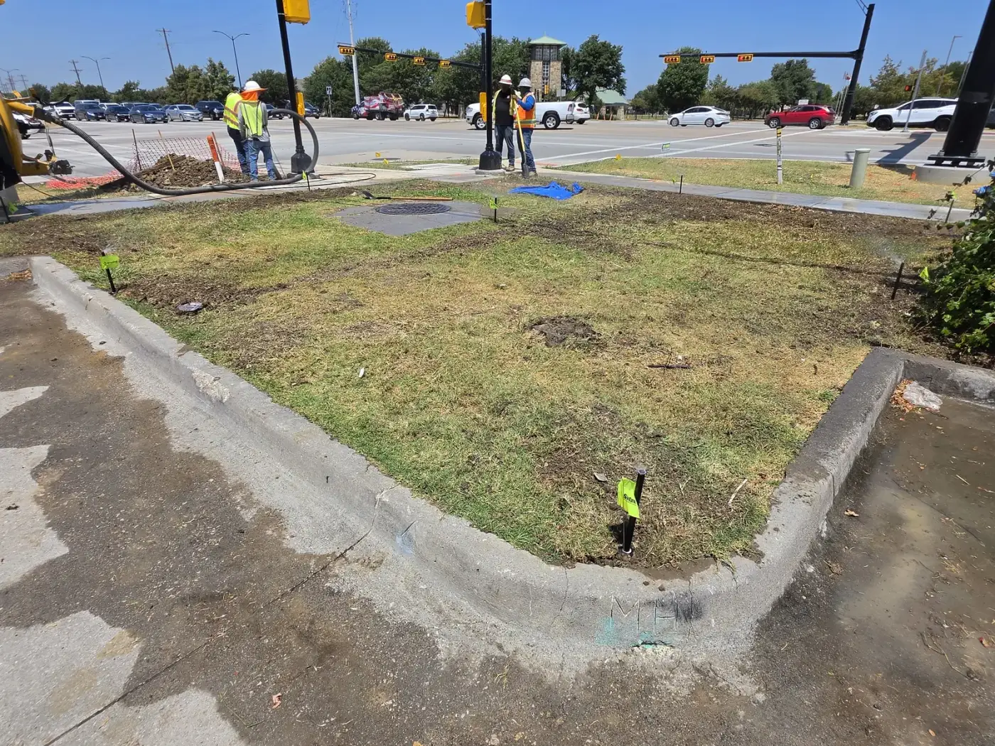 Godoy's Wolves crew working a commercial median irrigation job with utility locate flags and vacuum excavation at a signalised intersection