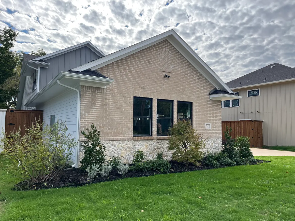 Brick and stone gable end of a finished new build with established green sod running to a black-mulched shrub bed cut in a clean curve