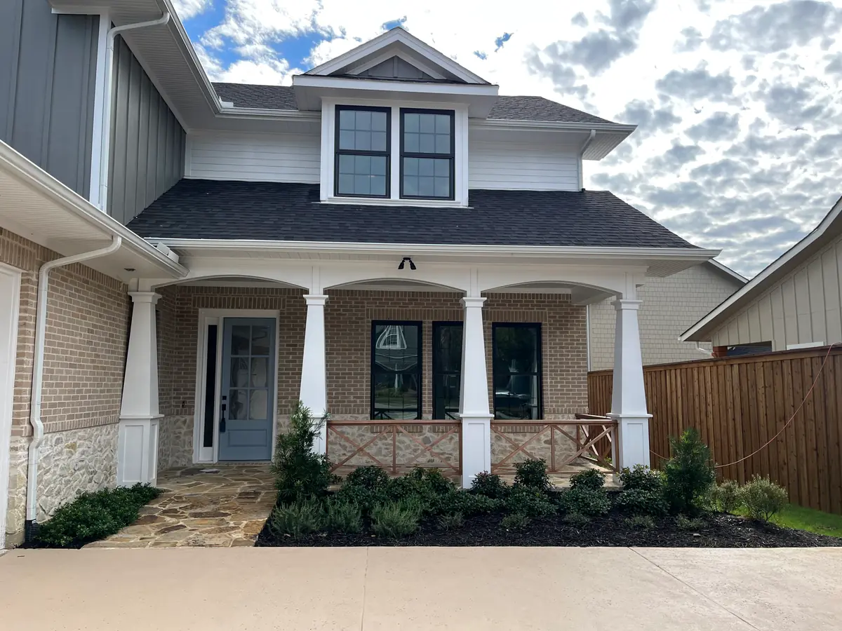 The same columned brick porch finished: flagstone walk set, foundation beds planted and topped in black mulch with a clean cut edge