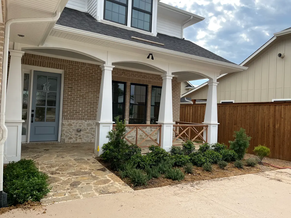 Flagstone entry walk laid to a columned brick porch with the foundation beds freshly planted in shrubs and rosemary, mulch not yet spread