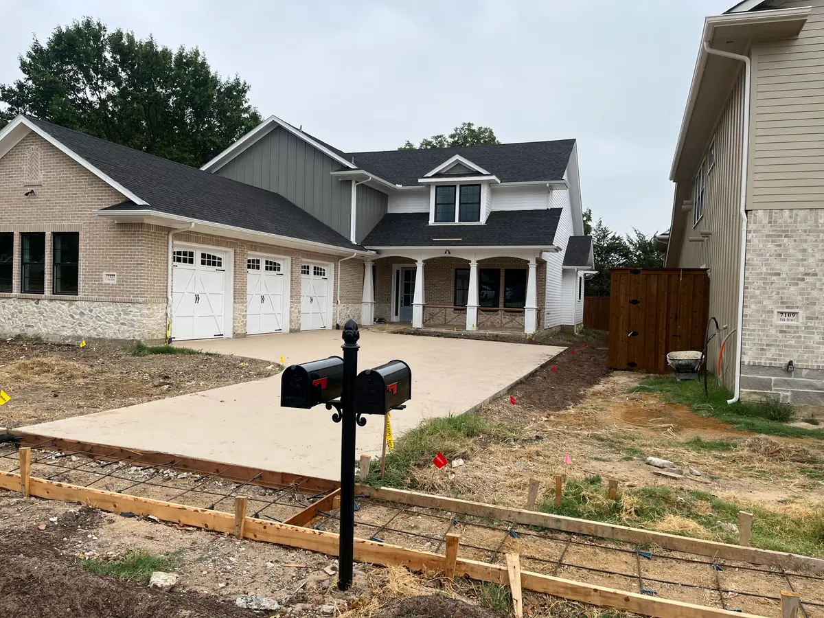 New build with the driveway poured and the front walk still in timber forms over rebar, marking flags across the bare lot and mailboxes set at the curb