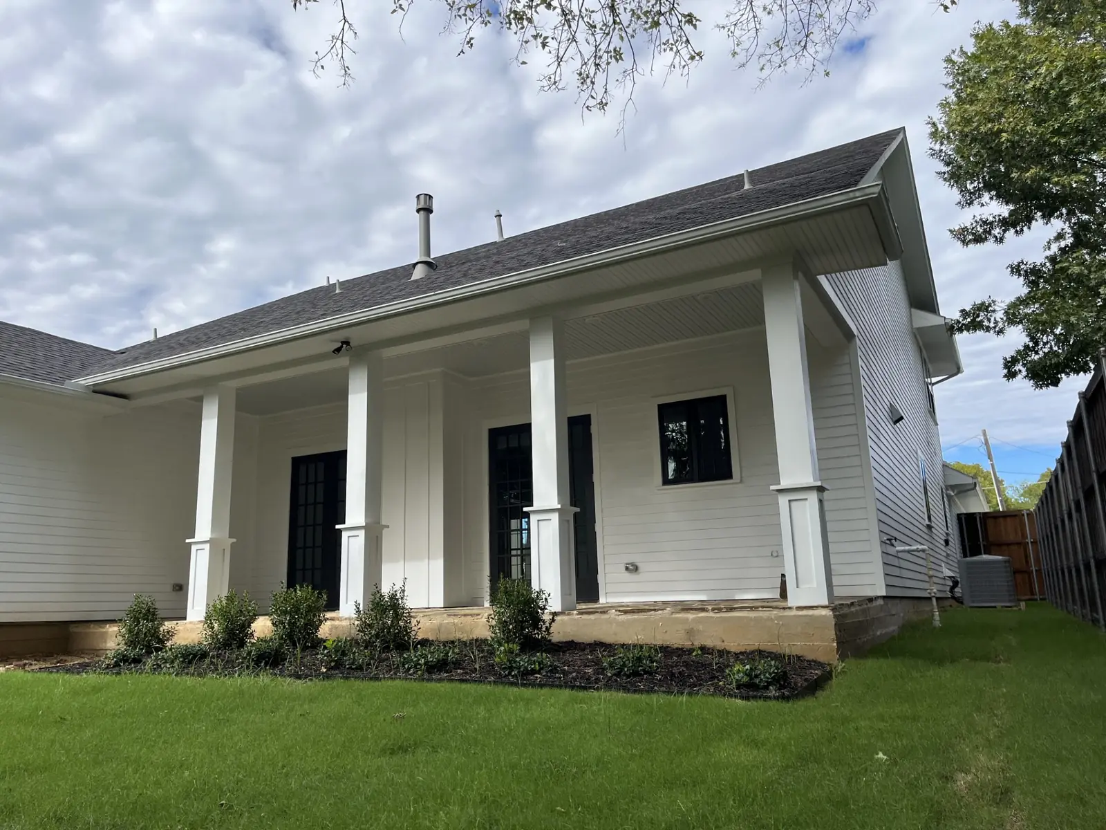 Finished front landscape on a new-construction home: fresh sod up to a mulched foundation bed of young shrubs, set against a white columned porch