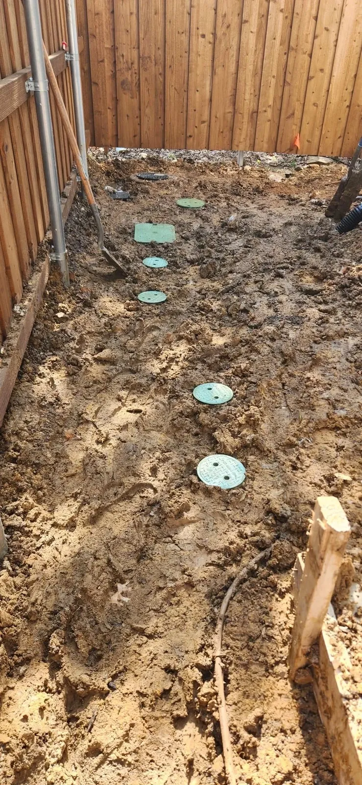 Irrigation valve boxes set into trenched ground along a fence line before backfill
