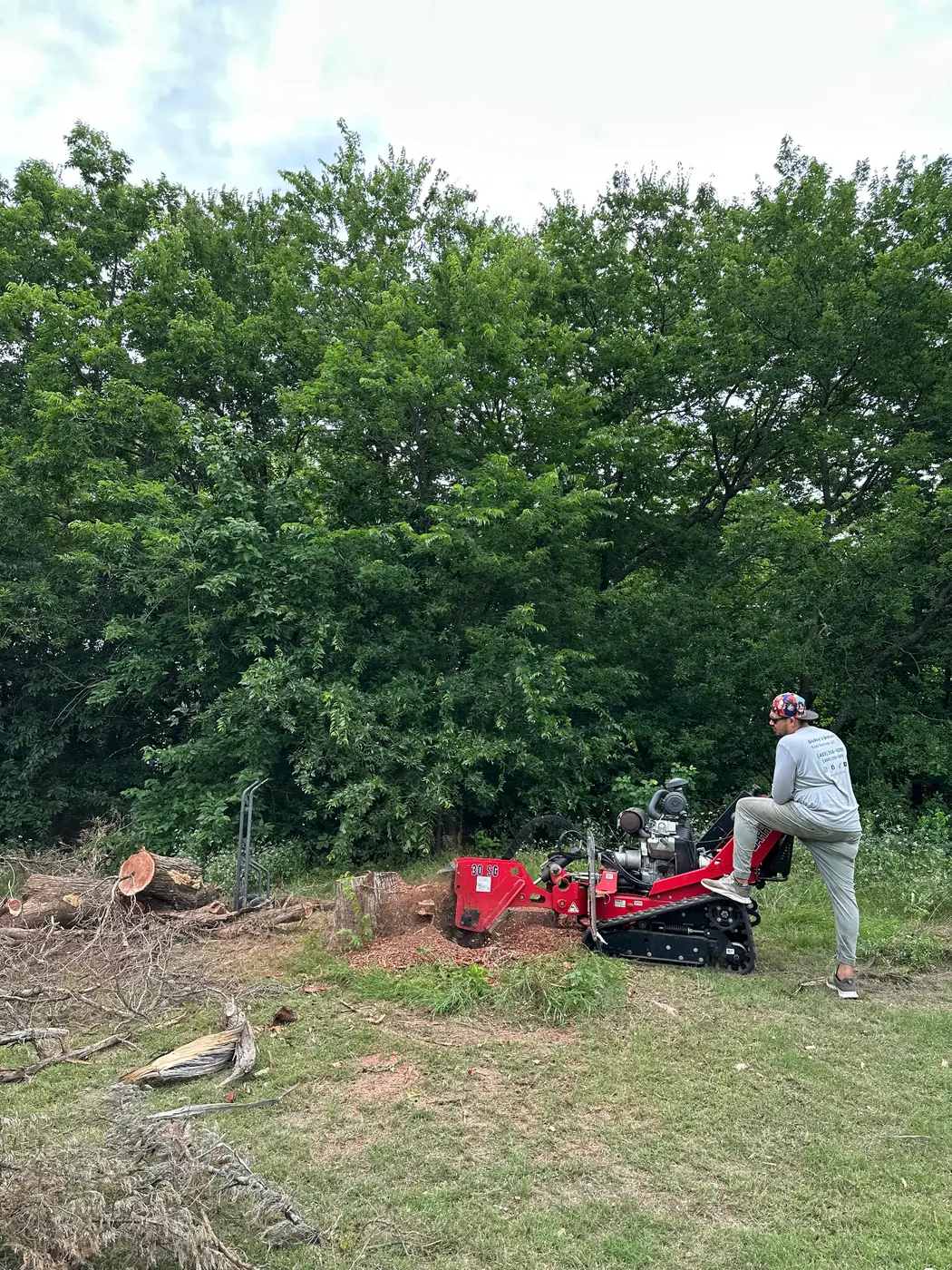 Stump grinder working a stump tight against a brick bed edge, fresh grindings filling the ring